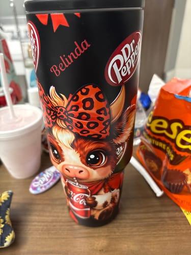 Customer's Personalized Dr Pepper Highland Cow 40oz Tumbler, featuring a cute cow design and custom name, on a table.