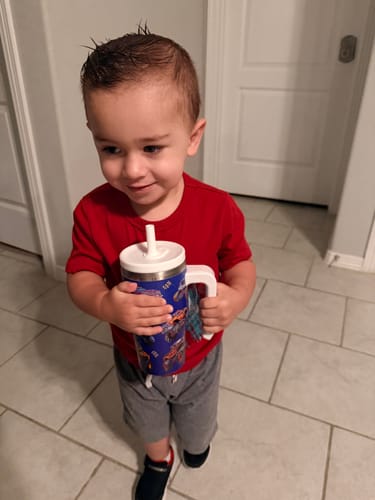 Customer's child happily holding a blue Monster Truck Spill Proof Kids CREWCUP with a white lid and straw