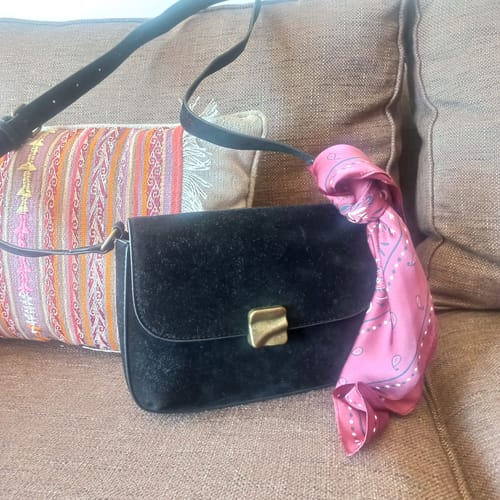 Customer's compacta Cartera Bandolera Fake Suede Woman, negra con detalle de pañuelo rosa sobre un sofá.