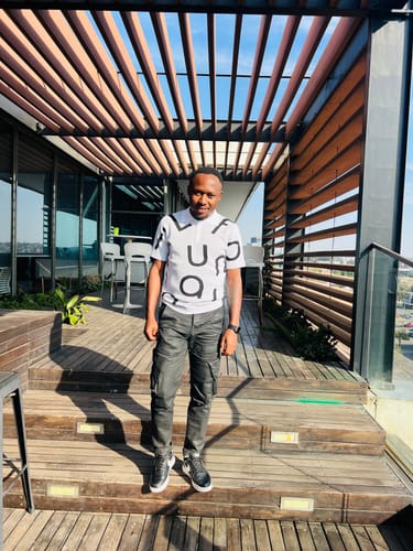 Customer wearing a white knit top with dark pattern standing on a wooden deck during the day.