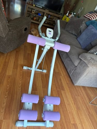 Customer's compact home exercise machine with lilac foam pads on a wood floor in a living room.