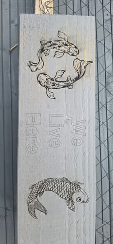 Customer's AtomStack Swift laser-engraved light wood board with three koi fish illustrations and text reading We Live Here.