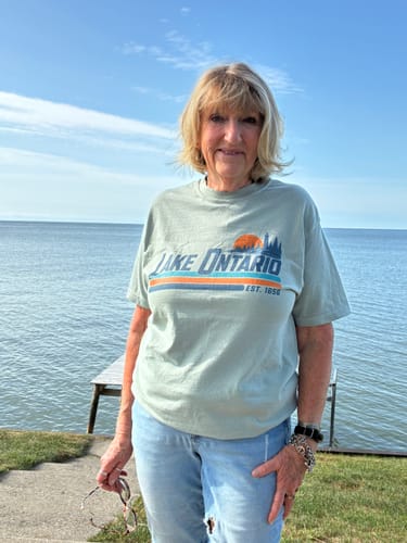 Customer's Lake Ontario Retro Stripe T-Shirt, light green, worn by a person outdoors near a lake.
