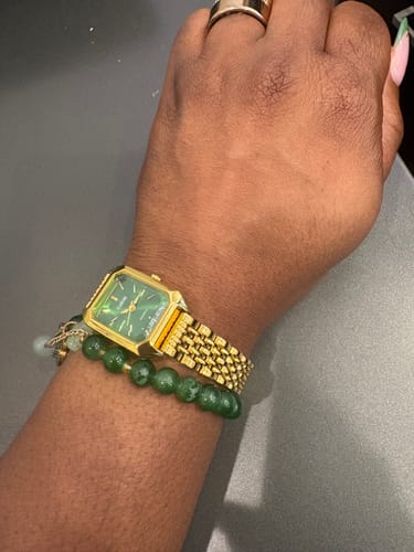 Customer's gold Claire De Mains watch with a green square face, worn on wrist with green beaded bracelets.