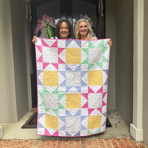 Customer's Cut Flowers Quilt showing a colorful star pattern, held up by two people.
