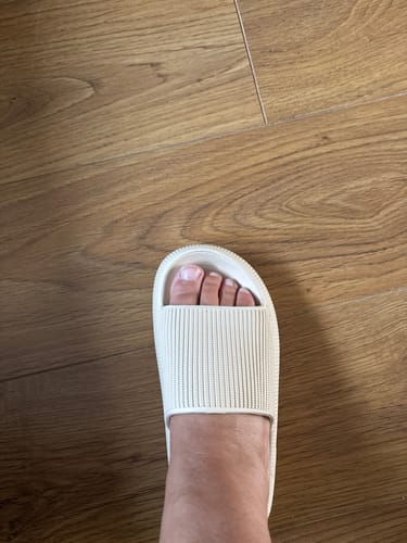 Customer's off-white HappyFlops slider worn on a wooden floor, showing a comfortable fit.