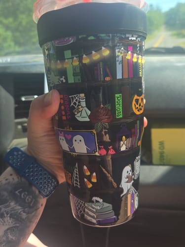 Reviewer's To-Go Buddy cup decorated with spooky illustrations of ghosts, pumpkins, and books, held in a hand.