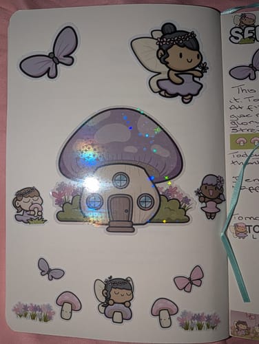 Customer's journal page decorated with holographic mushroom house, fairy, butterfly, and flower stickers from Ultimate Subscription.