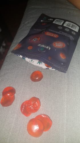 Kundenfoto der THC Spacejellies 2.0 Packung mit mehreren runden, orangefarbenen Gummibärchen auf einem grauen Untergrund.
