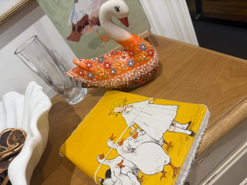 Customer's Waddlefolk fabric journal with a girl and geese, resting on a table near a decorative swan figurine.