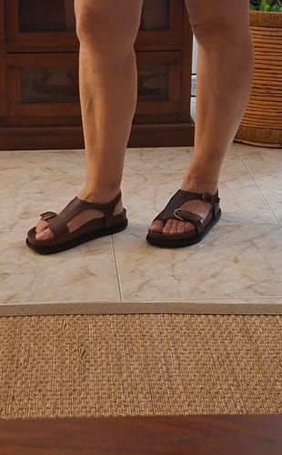 Customer's brown leather sandals on feet, standing on tile floor.
