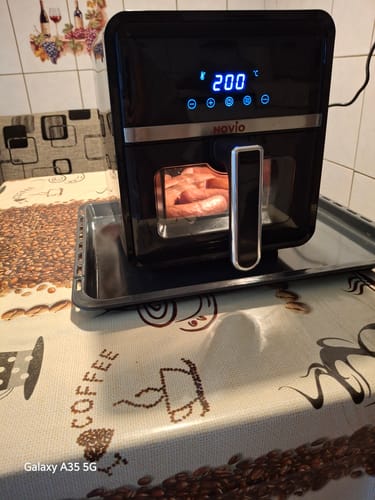 Reviewer's black Novio StonePro air fryer on a kitchen table, showing food cooking inside through the glass window.