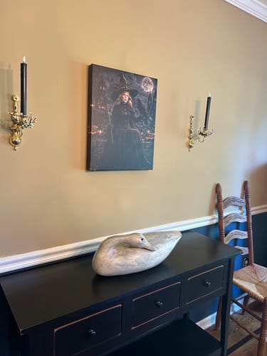 Customer's Raven Witch personalized portrait hung on a wall with black candles and a carved bird figurine.