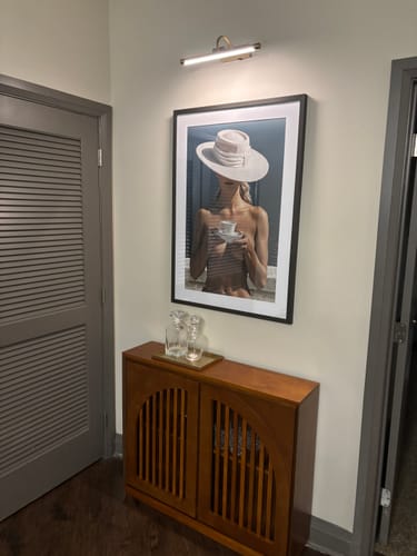 Customer's White Gallery Mat Board framing artwork hanging on a light wall above a wooden cabinet.