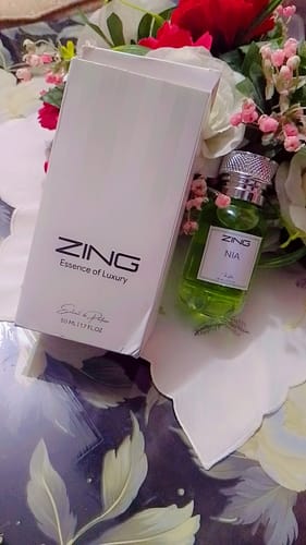 Customer's NIA floral fragrance bottle standing next to its elegant white box amidst decorative flowers.