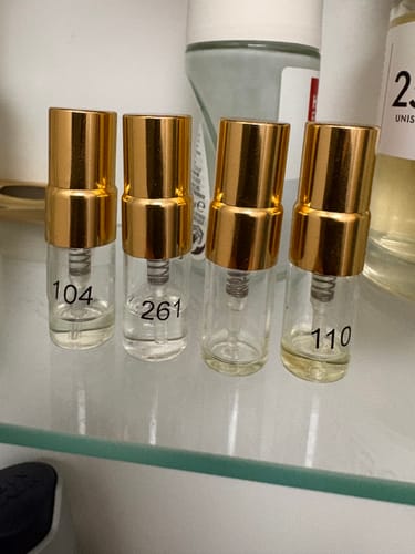 Reviewer's Tester Set featuring four small clear glass perfume vials with gold caps standing on a shelf.