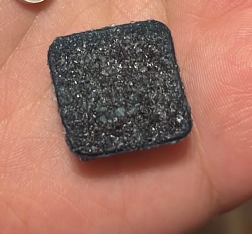 Customer's Blue Razz Gummies, a single sugar-coated dark blue square edible held in the palm of a hand.