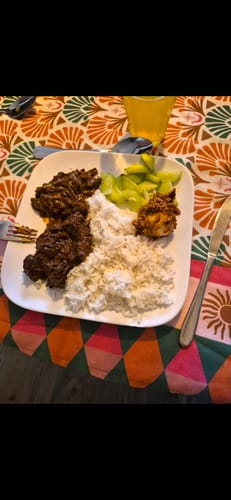 Customer's Rendang Bomb gerecht op een wit bord met witte rijst en groene groenten op een kleurrijk tafelkleed.