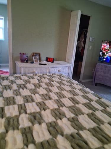 Customer's Hugs Check Sage Blanket featuring a plush, checkered pattern laid over a bed in a bedroom.