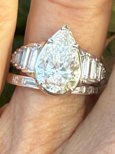 Customer's platinum ring with a large pear-shaped center stone and baguette accent stones on a person's finger