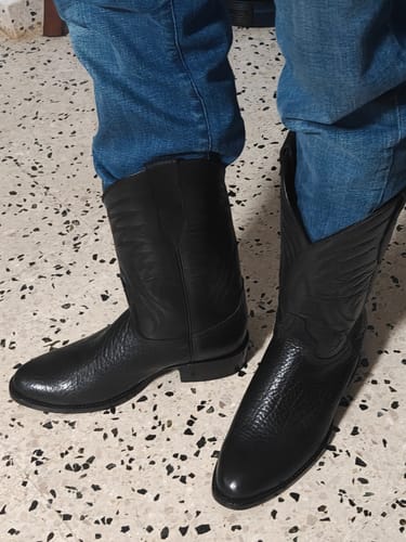 Customer's black cowhide leather boots on a person's feet, showing textured leather and stitching details.