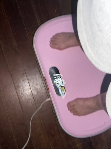 Customer's feet standing on the pink CV40 Vibration Plate for weight loss, placed on a wooden floor.