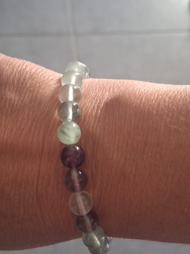 Customer's bracelet fluorine, worn on a wrist, featuring spherical beads in shades of green and purple.