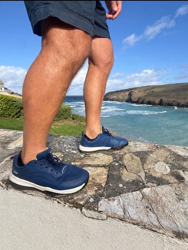 Customer's dark blue CUURT Muuv court shoes being worn outdoors on a stone wall overlooking the ocean.