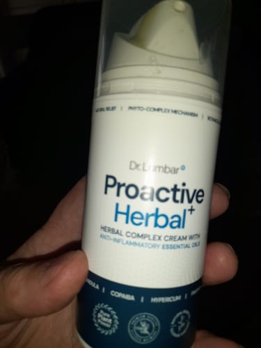 Customer's hand holding a white bottle of Proactive Herbal+ cream for muscle and joint comfort.