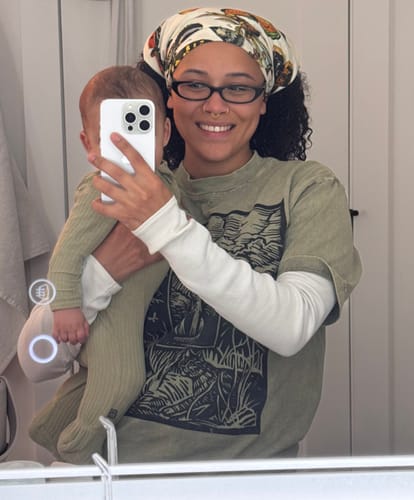Customer's Pinned Bandana worn as a headwrap, featuring a patterned butterfly print while holding a baby.