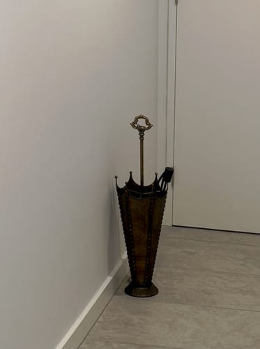Customer's Louna umbrella stand with antique gold finish placed in a corner against a white wall.