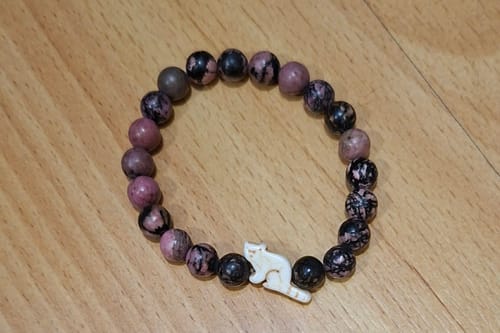 Customer's Dash Bracelet with black and purple stone beads and a small white red panda charm on a wooden surface.