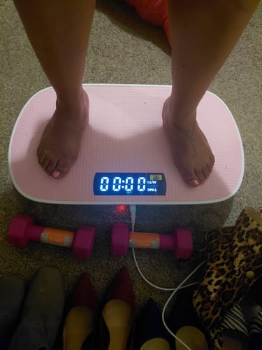Customer's feet on a pink CV30 Pro vibration plate with two small pink dumbbells on the floor nearby.