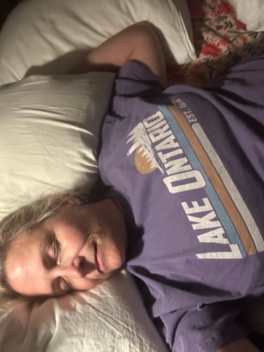 Customer's purple Lake Ontario Retro Stripe T-Shirt, worn by person lying in bed with head on a white pillow.