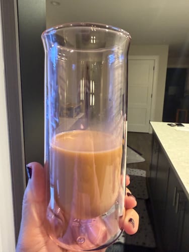 Customer's hand holding a FLUR Iced Coffee Glass filled with brown coffee, showing the clear double-walled design.
