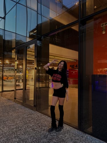 Customer's JR Nine To Five siyah boxy fit tişört giyen bir kişi modern bir binanın önünde poz veriyor.