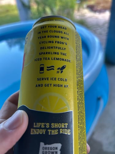 Reviewer's hand holding a yellow Sparkling THC Iced Tea Lemonade can, with text visible in front of a blue pool.