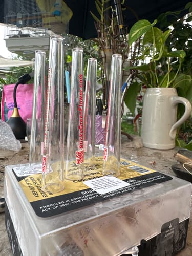 Customer's Colombia Gold pre rolls in clear plastic tubes resting on a box in an outdoor setting.