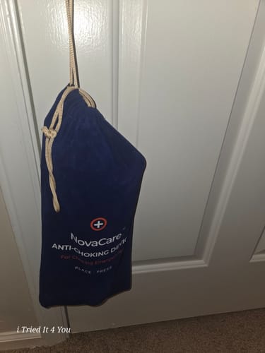 Reviewer's NovaCare Emergency Access Pouch in blue fabric with drawstring, hanging from a door handle.