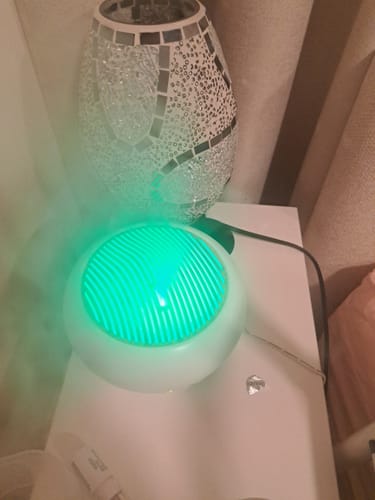 Customer's Sakura Aroma diffuser glowing with a bright green LED light on a table next to a decorative lamp.