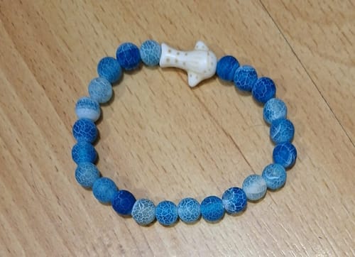 Customer's The Quest Bracelet featuring blue, textured beads and a small, white whale shark charm on a wooden surface.
