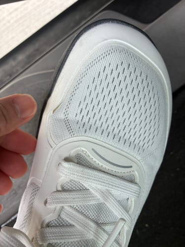 Customer's white CUURT Muuv court shoe with a hand pointing to a small tear near the toe box.