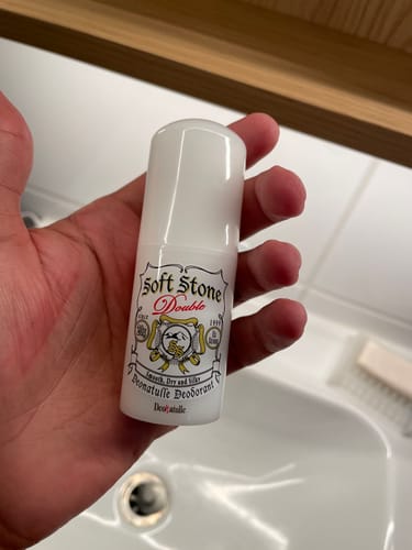 Reviewer's hand holding a Deonatulle Soft Stone Double deodorant stick in a bathroom setting.