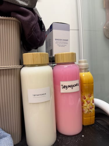 Customer's glass bottles with Tøymykner labels, standing on a surface among other household laundry products.