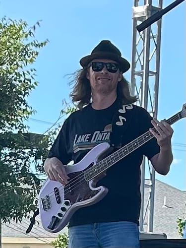 Customer's Lake Ontario Retro Stripe T-Shirt worn by a musician playing a bass guitar on a festival stage.