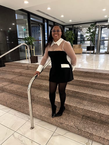 Customer's Ponte Shirting Mini Dress with sheer tulle décolletage and black stockings, standing on stairs.