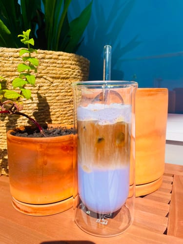 Customer's FLUR Iced Coffee Glass containing a layered purple and brown coffee drink with a glass straw on a patio table.