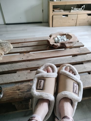 Customer's beige HappyFluff slippers with soft lining on feet, worn while relaxing on a wooden pallet table.