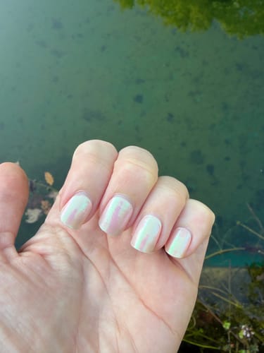 Reviewer's hand displaying Pink Champagne UV Gel Nail Wraps with a glazed effect against a blurry outdoor background.