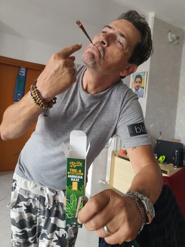 Customer's THC-A Pre-Roll Cali Blend packaging held while the reviewer holds a lit pre-roll cone in their mouth.